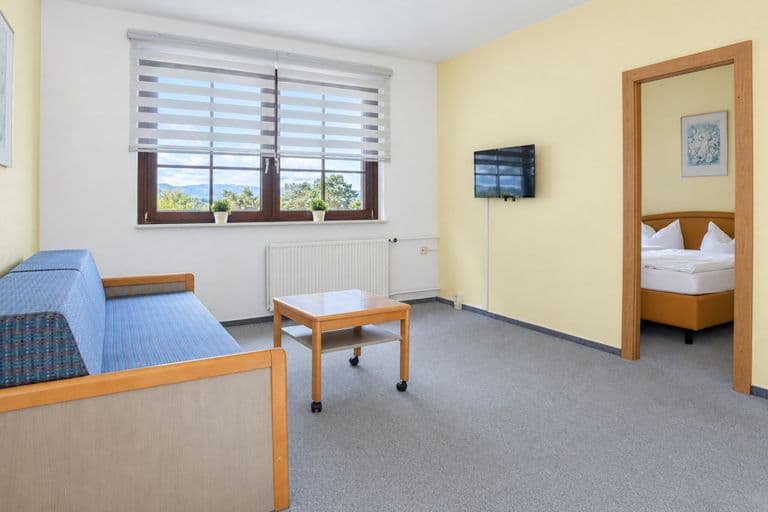 Wohnbereich der Junior-Suite mit Schlafsofa und Couchtisch, durch die offene Tür der Schlafraum