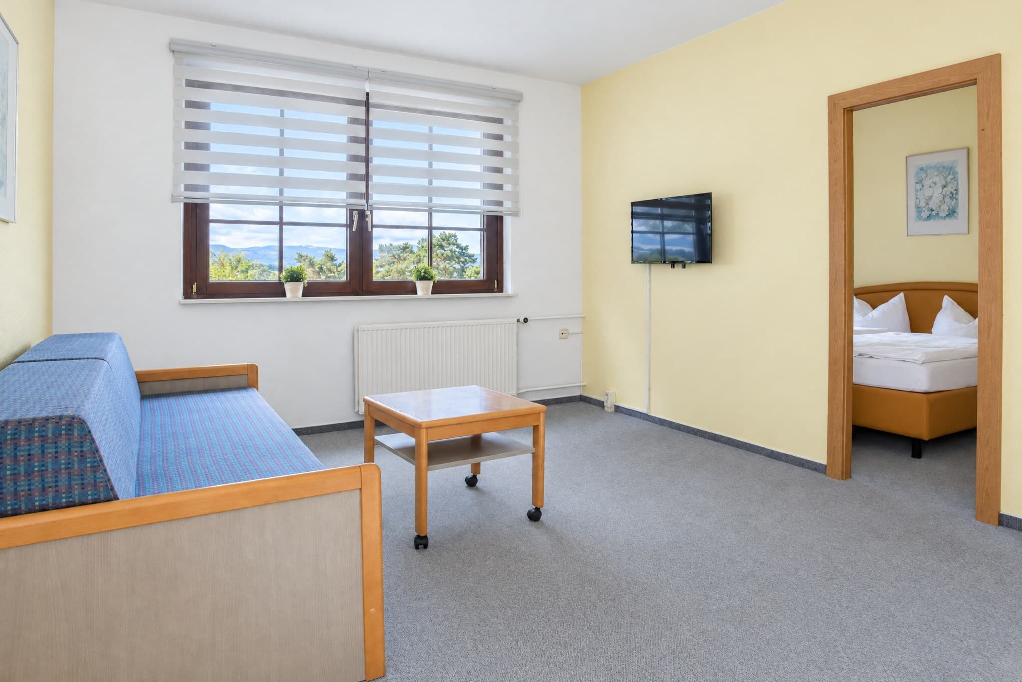 Wohnbereich der Junior-Suite mit Schlafsofa und Couchtisch, durch die offene Tür der Schlafraum