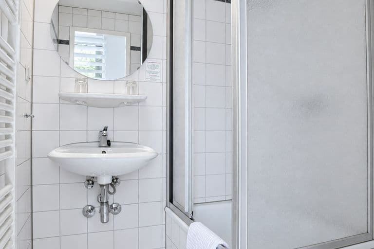 Bad des Standardzimmers mit Dusche, Waschbecken und rundem Spiegel