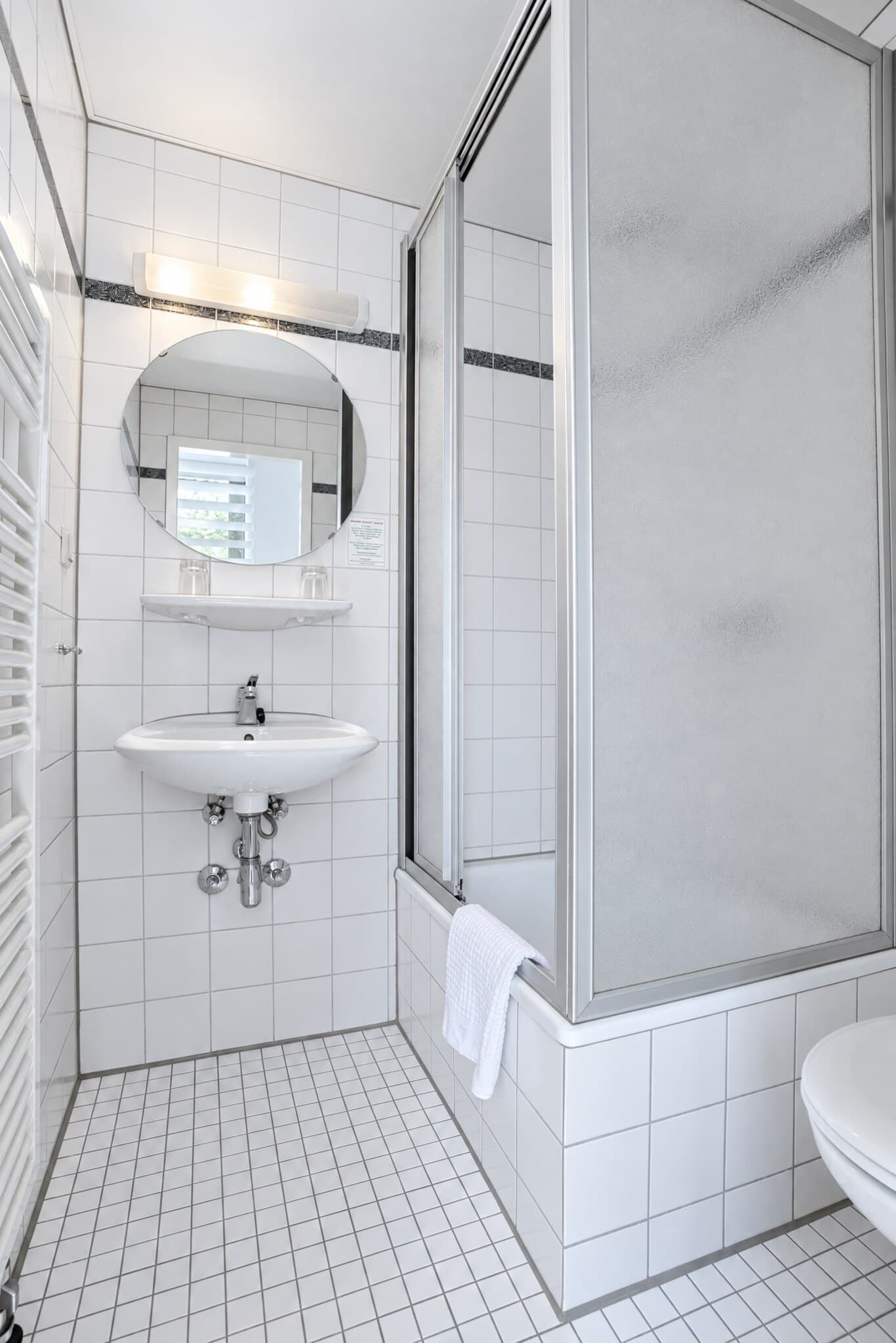 Bad des Standardzimmers mit Dusche, Waschbecken und rundem Spiegel
