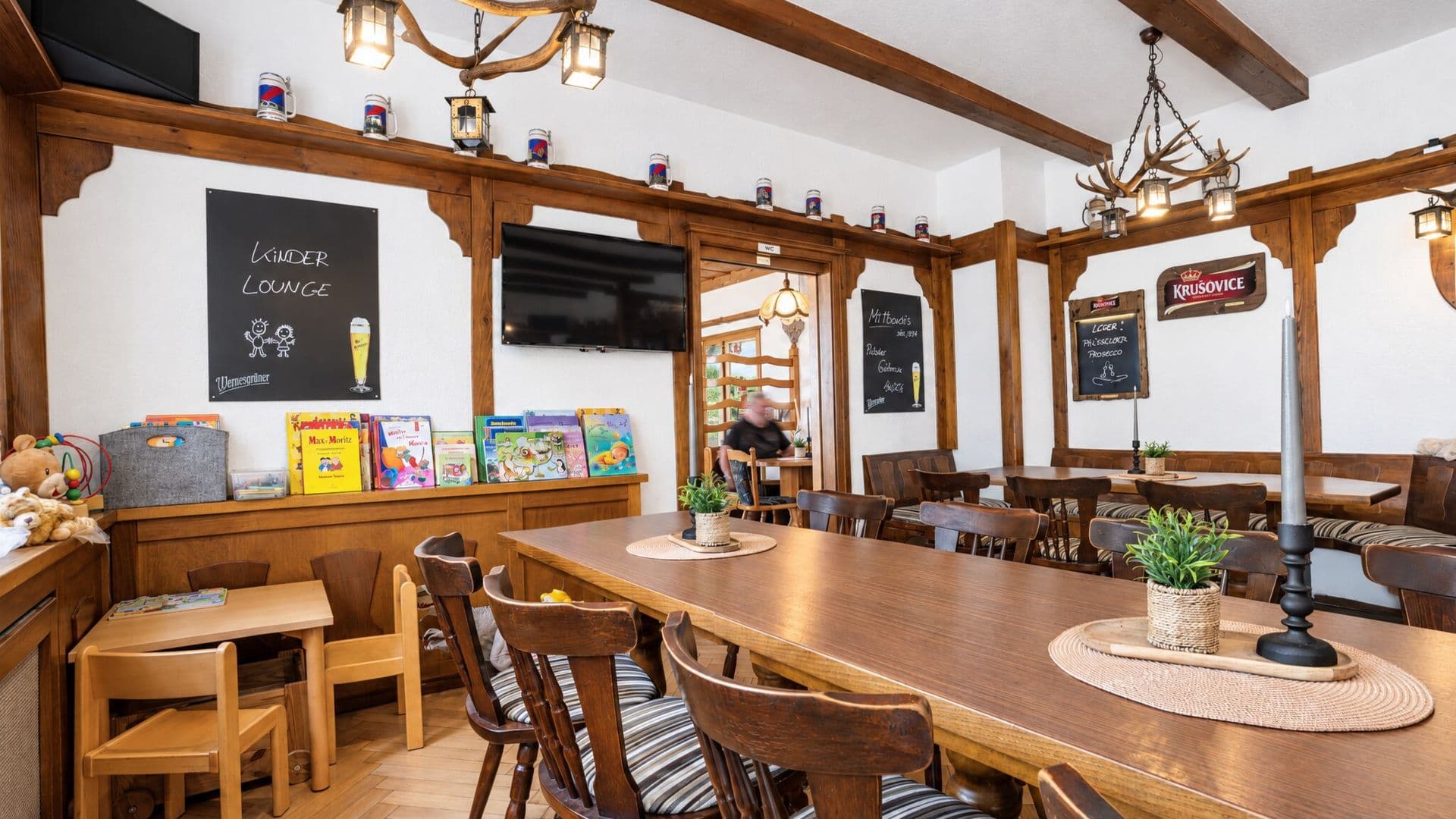 Jägerzimmer mit Geweihleuchtern, langer Holztafel und Kinder-Lounge mit Büchern