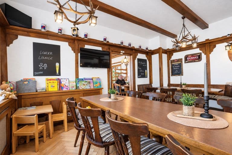 Jägerzimmer mit Geweihleuchtern, langer Holztafel und Kinder-Lounge mit Büchern